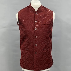Könnte beinhalten: Eine bordeauxfarbene Weste mit Stehkragen und geometrischem Muster. Die Weste hat eine Knopfleiste, zwei Vordertaschen und wird auf einer weißen Schaufensterpuppe präsentiert. Der Stoff hat einen dezenten Glanz.