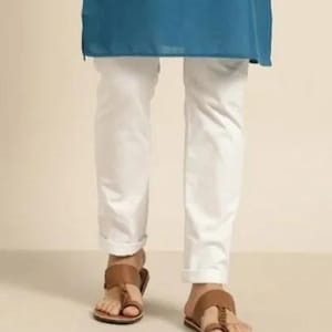 Könnte beinhalten: Weiße Hose mit umgeschlagenem Saum und braunen Ledersandalen. Die Sandalen haben eine Zehenschlaufe und einen Riemen über dem Fuß. Die Hose wird mit einem türkisfarbenen Oberteil kombiniert.
