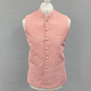 May include: A pink vest with a floral pattern, displayed on a mannequin. The vest has a mandarin collar, a breast pocket, and gold-colored buttons. The vest is sleeveless and appears to be made of a textured fabric.