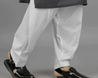 Op de afbeelding: Witte, loszittende broek gecombineerd met zwarte leren sandalen. De sandalen hebben een gespsluiting en een textuurzool. De outfit wordt gecompleteerd met een donkere top, wat zorgt voor een eenvoudige maar stijlvolle look.