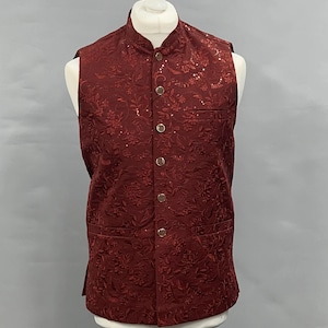 Peut inclure: Un gilet bordeaux avec un motif floral et des boutons dorés. Le gilet a un col mandarin et deux poches avant. Le vêtement est présenté sur un mannequin. Le gilet est un vêtement formel.