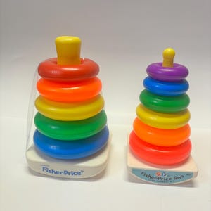 May include: Two Fisher-Price stacking ring toys. The larger ring is red, orange, yellow, green, and blue. The smaller ring is purple, blue, green, yellow, and orange. Both rings have a white base with the Fisher-Price logo.