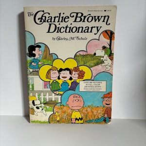 May include: A vintage copy of "The Charlie Brown Dictionary" by Charles M. Schulz. The cover features colorful illustrations of Charlie Brown, Snoopy, Lucy, and other Peanuts characters. The book is a Scholastic Book Services edition.