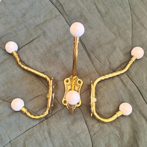 May include: Set of three decorative brass wall hooks with white spherical finials. The hooks have a twisted design and are mounted on ornate brass backplates. The hooks are designed for hanging items.
