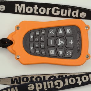 May include: Orange and black remote control with a keypad and a directional pad. The remote control has the text "MotorGuide" printed on it. The remote control is attached to a black lanyard with the text "MotorGuide" printed on it.