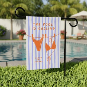Könnte beinhalten: Eine Gartenflagge mit blau-weiß gestreiftem Hintergrund und dem Text "THE POOL IS CALLING". Die Flagge zeigt orangefarbene Bikini-Illustrationen, die an einer Wäscheleine hängen. Darunter steht der Text "SAVOR THE SUMMER".