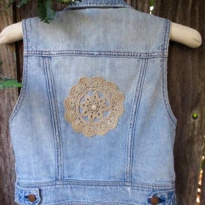 Pu&ograve; includere: Un giubbotto di jeans blu chiaro con un design in pizzo all'uncinetto sul retro.