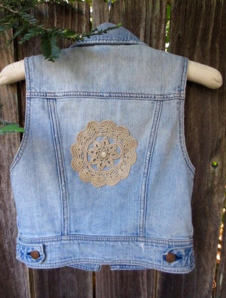 Pu&ograve; includere: Un giubbotto di jeans blu chiaro con un design in pizzo all'uncinetto sul retro.