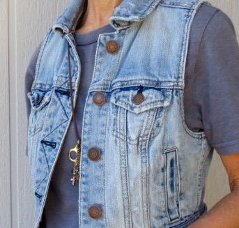 Pu&ograve; includere: Un giubbotto di jeans blu chiaro con bottoni marroni e una collana di cuoio marrone con ciondoli.