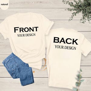 May include: Two natural-colored short-sleeve t-shirts displayed together. One shirt features the black text FRONT YOUR DESIGN, while the other displays the black text BACK YOUR DESIGN. A pair of blue denim jeans is folded and placed over the first shirt.