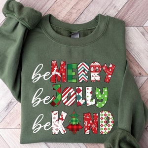 May include: A green sweatshirt with the text "be merry be jolly be kind" in colorful, patterned letters. The letters are decorated with Christmas-themed designs, including snowflakes, candy canes, and Christmas trees.