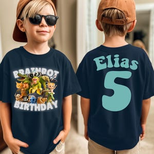 May include: Navy blue t-shirt with a colorful graphic featuring cartoon characters and the text "BRAINROT BIRTHDAY" on the front. The back of the shirt displays the name "Elias" and the number "5" in light blue.
