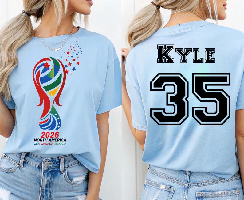 May include: Light blue t-shirt featuring a colorful graphic with the text "2026 NORTH AMERICA USA CANADA MEXICO" on the front. The back of the shirt displays the name "KYLE" above the number "35" in black.