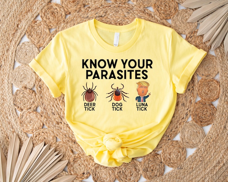 May include: A yellow t-shirt with the text "KNOW YOUR PARASITES" above illustrations of a deer tick, dog tick, and a cartoon of a person. The shirt is folded at the bottom.