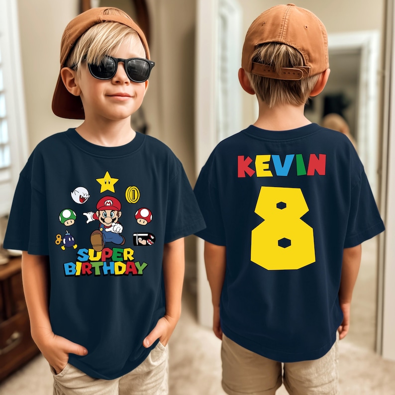 May include: Navy blue t-shirt featuring a Super Mario graphic with the text "SUPER BIRTHDAY" and the number 8. The back of the shirt displays the name "KEVIN" and the number 8 in yellow.