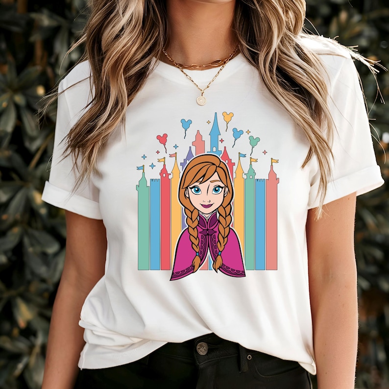 May include: White t-shirt with a colorful illustration of a cartoon girl with red hair and a purple cape in front of a castle with rainbow colored towers and Mickey Mouse balloons.