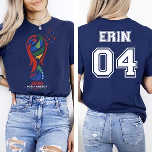 May include: Navy blue t-shirt with a colorful graphic and the text "2026 NORTH AMERICA USA CANADA MEXICO" on the front. The back of the shirt displays the name "ERIN" and the number "04" in white.