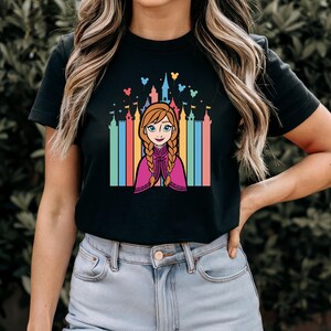 May include: Black t-shirt featuring a colourful graphic of Anna from Frozen in front of a rainbow castle with Mickey Mouse balloons.