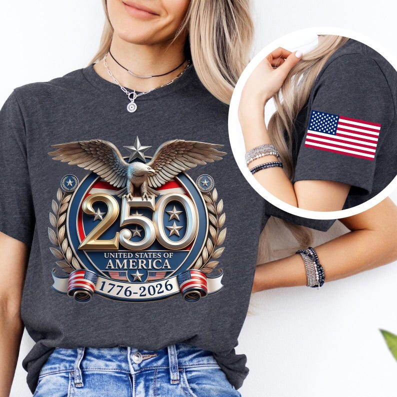 May include: Dark gray t-shirt featuring a patriotic design celebrating the United States of America's 250th anniversary. The design includes an eagle, stars, and the American flag. The sleeve has a small American flag patch.