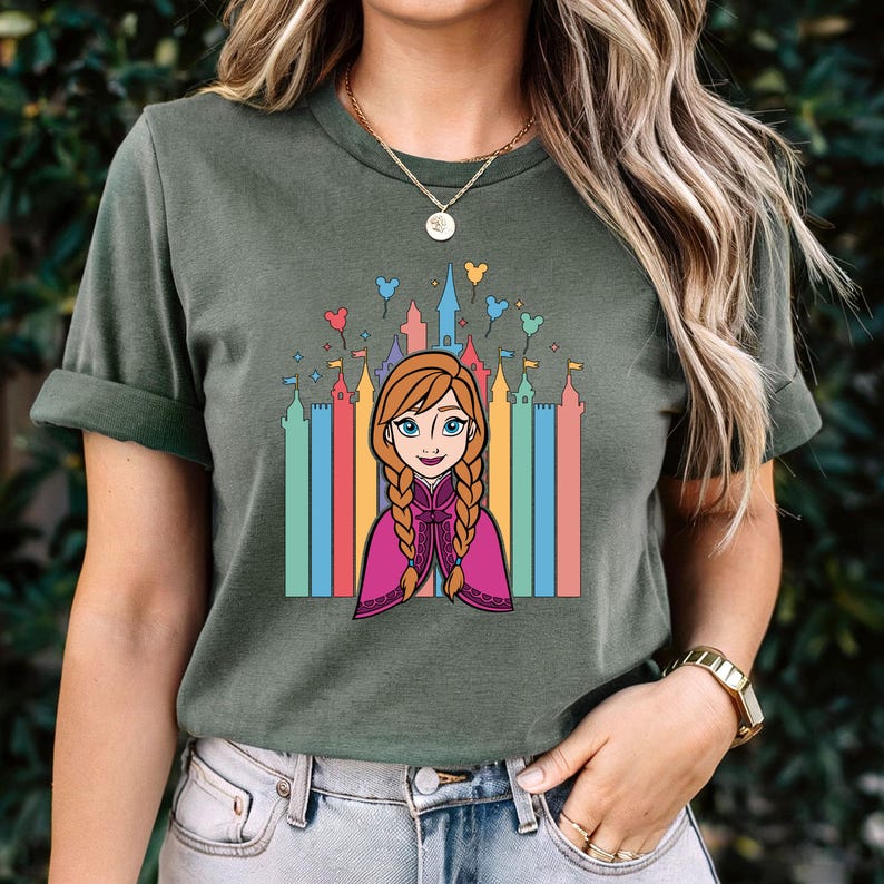 May include: A green t-shirt featuring a cartoon image of Anna from Frozen in front of a rainbow-coloured castle with balloons.