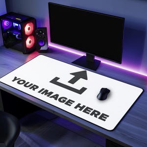 Op de afbeelding: Witte rechthoekige muismat met de tekst "YOUR IMAGE HERE" en een zwart uploadpictogram. Een zwarte computermuis ligt op de mat. Een computermonitor, een luidspreker en een computertoren staan op de achtergrond.