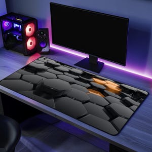 May include: Black and orange geometric pattern mouse mat. The mouse mat features a 3D hexagonal design with a glossy finish. The mat is rectangular and sits on a wooden desk, with a computer monitor and tower in the background.