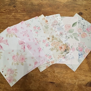 May include: A set of six rectangular paper dividers featuring various floral patterns in shades of pink, green, and cream. Each divider has a tab on the side and punched holes along the edge, displaying illustrations of roses, leaves, and ribbons.