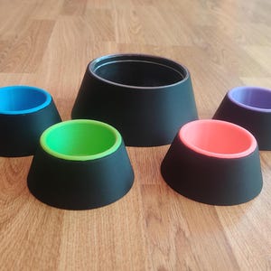 May include: Five black plastic pet bowls with different coloured inner bowls. The bowls are arranged in a semi-circle on a wooden surface. The colours of the inner bowls are blue, green, orange, purple, and black.