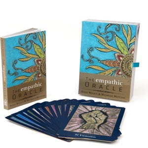 May include: A deck of The Empathic Oracle cards with a blue border and colorful illustrations. The cards are fanned out on a white surface. The box for the cards is in the background. The box is blue with a gold and green floral design. The text on the box reads "The Empathic Oracle" and "Steve Wilson & Michelle Motuzas".