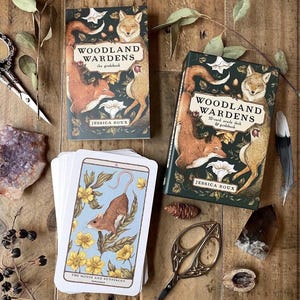 May include: An oracle deck and guidebook set titled "Woodland Wardens" by Jessica Roux. The deck features illustrations of a mouse and buttercups. The set includes a guidebook and a 52-card oracle deck, with a fox and other woodland creatures on the cover.