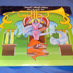 May include: A vintage vinyl record album cover featuring a colorful illustration of a trumpet, a woman in a flowing robe, and a man kneeling on a platform. The album title is "Muscle Shoals Horns doin' it to the bone".