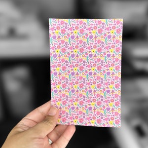 May include: A pink card with a repeating pattern of yellow, pink, and purple flowers and mushrooms.