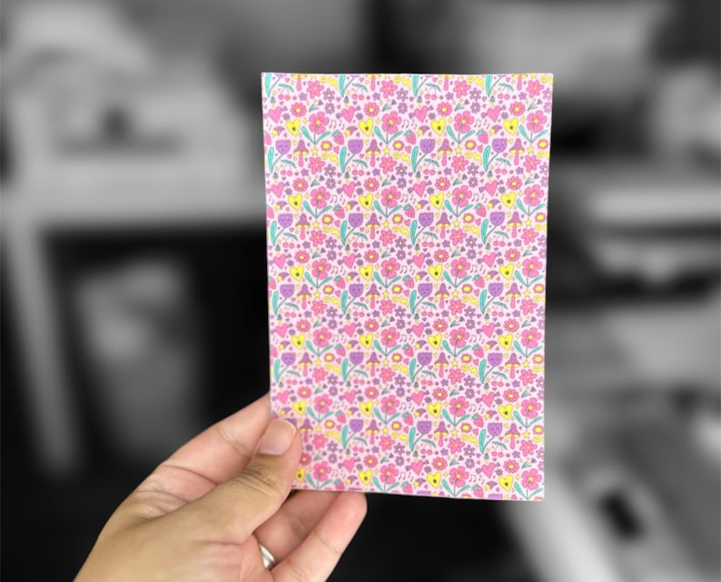 May include: A pink card with a repeating pattern of yellow, pink, and purple flowers and mushrooms.