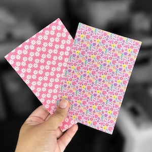 May include: Two sheets of pink patterned paper. One sheet has a white daisy pattern and the other has a pink, yellow, and purple floral pattern.