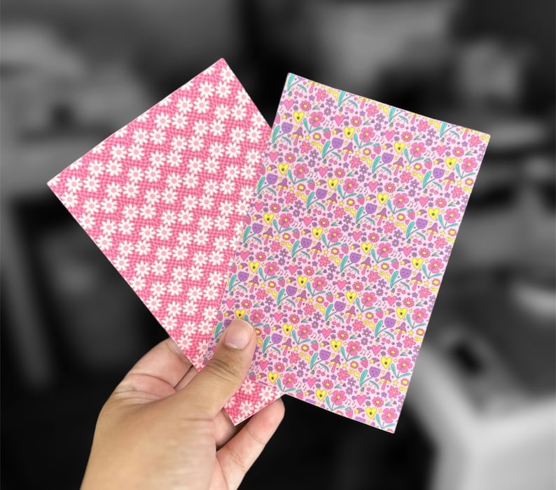 May include: Two sheets of pink patterned paper. One sheet has a white daisy pattern and the other has a pink, yellow, and purple floral pattern.