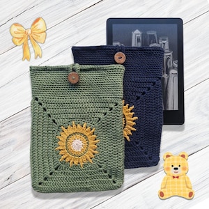 May include: Two crochet tablet cases, one green and one navy blue, with sunflower designs. Each case has a wooden button closure. A digital tablet is visible behind the cases. A yellow bow and a teddy bear sticker are also in the image.