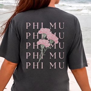 Op de afbeelding: Donkergrijs t-shirt met de tekst "PHI MU" en een roze bloemenontwerp. Het casual t-shirt is geschikt voor dagelijks gebruik. De foto is genomen op een strand.