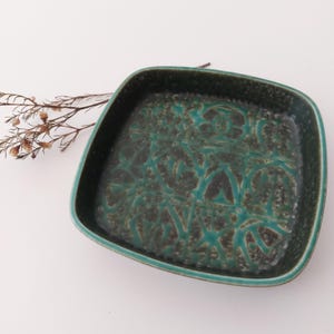 May include: A square ceramic dish with a teal green glaze and a brown pattern. The dish has a slightly raised rim.