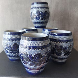 Może przedstawiać: Zestaw sześciu niebieskich i białych ceramicznych kubków z misternymi wzorami kwiatowymi. Kubki są wszystkie tego samego rozmiaru i kształtu i mają tradycyjny niemiecki styl.