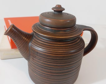 Puede incluir: Una tetera de cerámica marrón con tapa y diseño acanalado. La tetera tiene un pico y una asa.