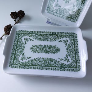 May include: Set of three white ceramic serving trays with green floral designs. The trays have a rectangular shape with rounded corners and handles on the sides.