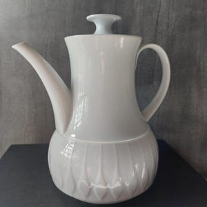 Puede incluir: Tetera de cerámica blanca con tapa y asa. La tetera tiene un diseño texturizado en la mitad inferior.