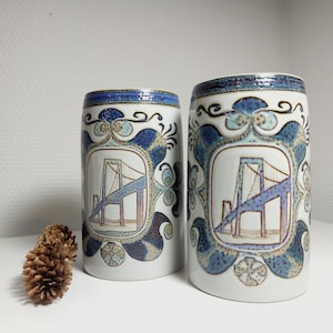 Puede incluir: Dos tazas de cerámica con un diseño azul y blanco que representa un puente. Las tazas tienen un fondo blanco con detalles azules y marrones.