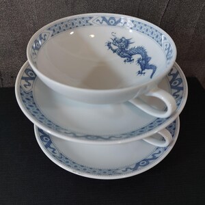 Könnte beinhalten: Drei weiße Porzellan-Teetassen mit blauen und weißen Drachenmotiven. Die Tassen sind übereinander gestapelt.