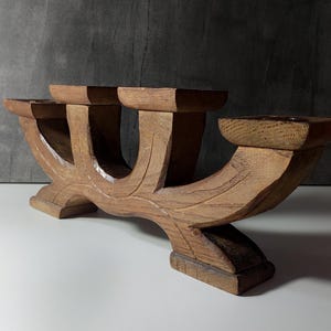 Può includere: Un candelabro in legno marrone caratterizzato da una base curva a più livelli con tre distinte piattaforme quadrate per candele. La venatura del legno è visibile su tutta la struttura, che poggia su due piedi robusti dal design intagliato.