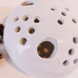 May include: White ceramic sphere with multiple round holes of varying sizes. The sphere is a decorative object with a smooth, glossy finish.