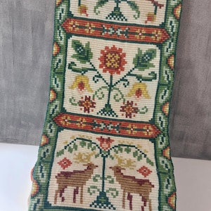 Könnte beinhalten: Rechteckige Tapisserie mit cremefarbenem Hintergrund und grünem Rand. Die Tapisserie zeigt drei Tafeln mit Blumen- und Tiermotiven in Rot, Gelb und Braun. Die Tapisserie wird auf einem schwarzen Metallständer präsentiert.