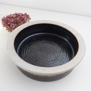 May include: A round ceramic bowl with a black interior and a white rim. The bowl has a textured surface and a slightly raised lip.