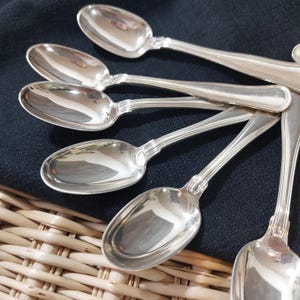 May include: A set of eight silver teaspoons with a polished finish. The spoons are arranged in a fan shape, with the handles pointing outwards.