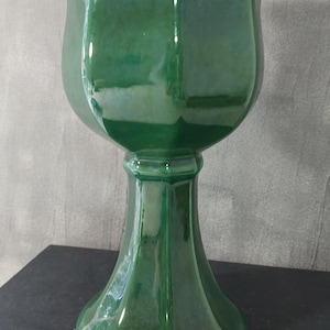 Puede incluir: Un jarrón de cerámica verde esmeralda brillante con una parte superior acampanada y una base de pedestal. El jarrón tiene una superficie lisa y reflectante y una forma clásica y elegante. Es un artículo decorativo, adecuado para exhibir flores o como pieza de acento independiente.